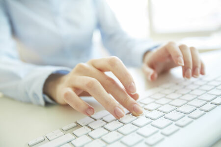 Eine Frau tippt mit beiden Händen auf einer weißen Computertastatur